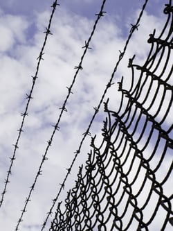 Keep out -- chain link fence with barbed wire against partly cloudy sky